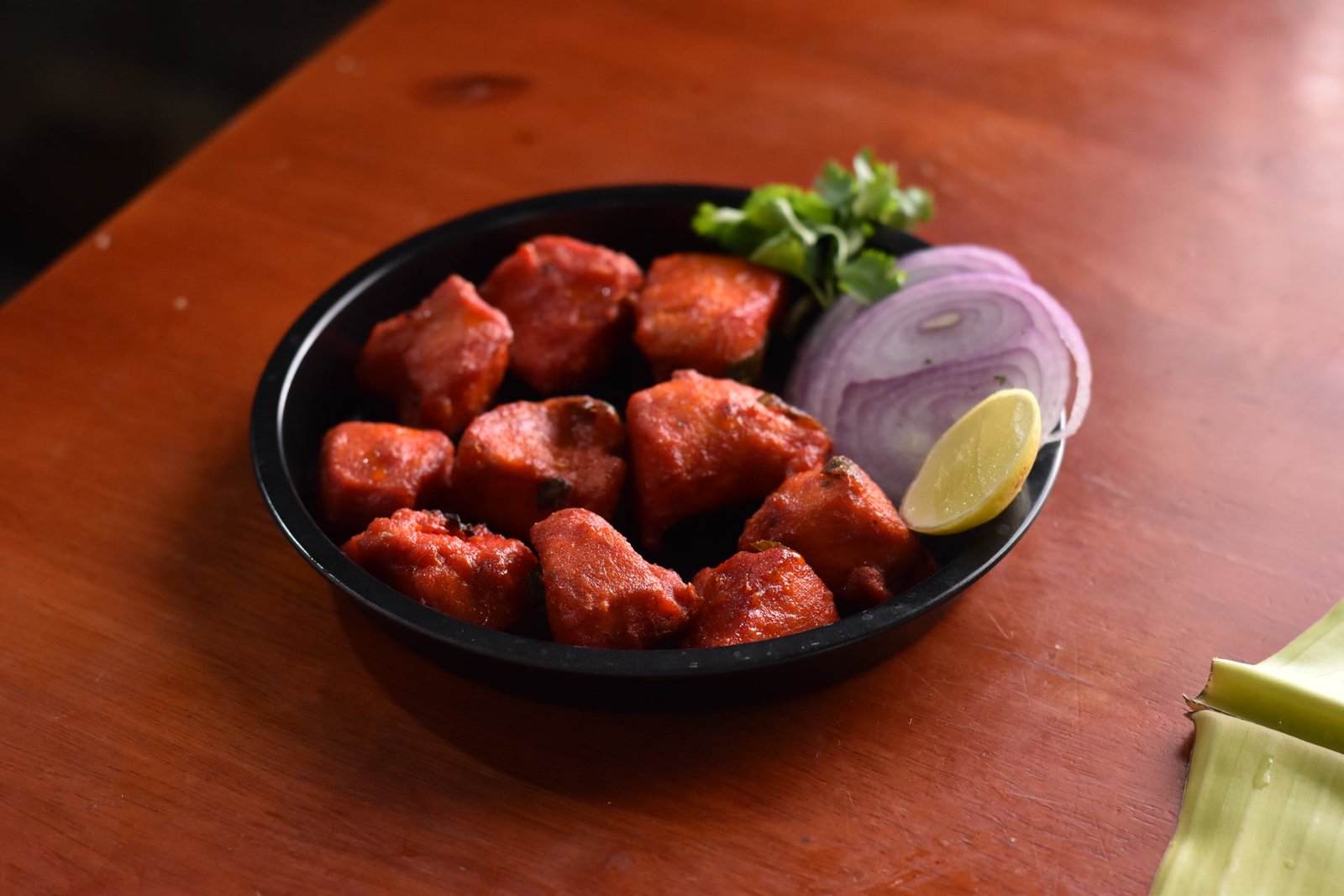 Chicken 65 served in a black dish with onion and lemon
