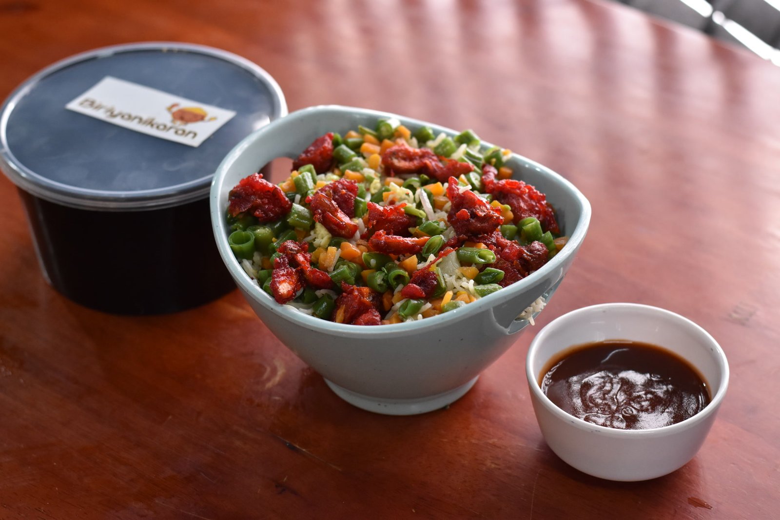 Fried rice with chilli chicken in a bowl beside a sealed Biriyanikaran container